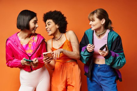 Tres mujeres de diversas etnias de pie juntas, mirando atentamente la pantalla de un teléfono celular.