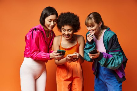 Drei unterschiedliche Mädchen, darunter kaukasische, asiatische und afroamerikanische, drängten sich aneinander und blickten auf ein Handy mit orangefarbenem Hintergrund..