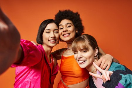 Téléchargez les photos : Un groupe de femmes diverses capturant des moments avec un téléphone portable sur fond de studio orange. - en image libre de droit