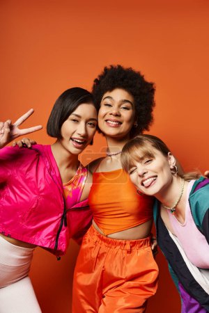 Foto de Un grupo diverso de mujeres están hombro con hombro, mostrando belleza y fuerza sobre un fondo naranja vivo. - Imagen libre de derechos