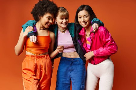 Trois femmes d'origines culturelles différentes debout ensemble sur un fond de studio orange.