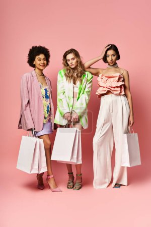 Three women of different ethnicities standing together, holding shopping bags on a pink background.