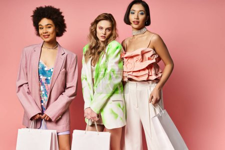 Drei unterschiedliche Frauen, kaukasische, asiatische und afroamerikanische, stehen mit Einkaufstaschen vor rosa Studiohintergrund zusammen..