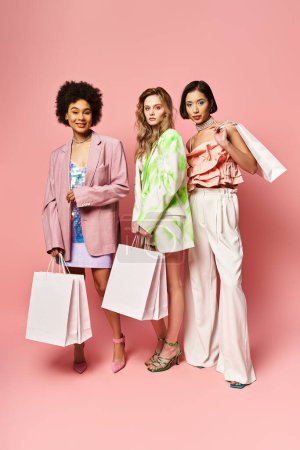 Three women of diverse backgrounds standing together, holding vibrant shopping bags against a pink background.