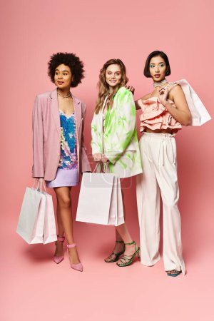 Tres mujeres diversas están juntas sosteniendo bolsas de compras sobre un fondo rosado, exudando alegría y satisfacción.