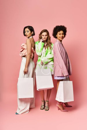 Three women of different ethnicities holding shopping bags on a pink background.