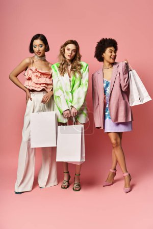 Drei unterschiedliche Frauen stehen nebeneinander, lächeln und halten Einkaufstüten vor rosa Hintergrund..