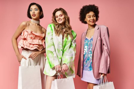 Tres mujeres de diversos orígenes de pie juntos, sosteniendo bolsas de compras contra un vibrante telón de fondo rosa.