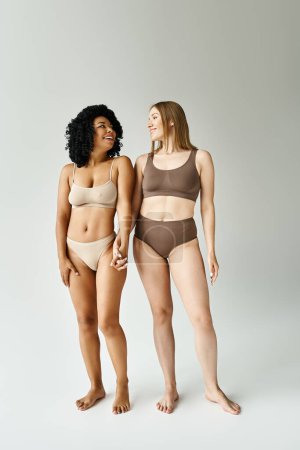 Two beautiful diverse women standing in cozy pastel underwear.