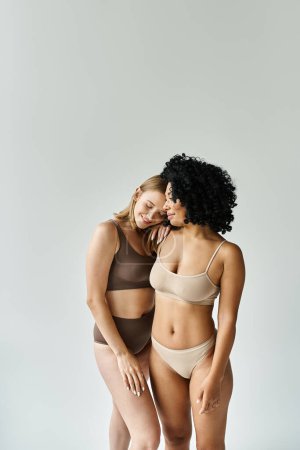 Foto de Dos hermosas y diversas mujeres de pie una al lado de la otra en ropa interior de pastel acogedor. - Imagen libre de derechos