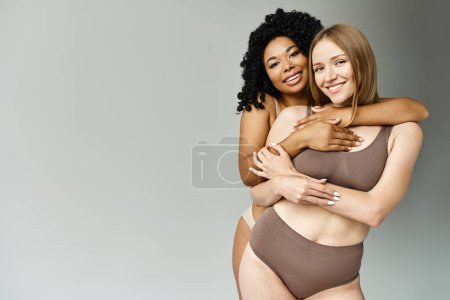 Dos hermosas y diversas mujeres en trajes de baño pastel abrazándose calurosamente.