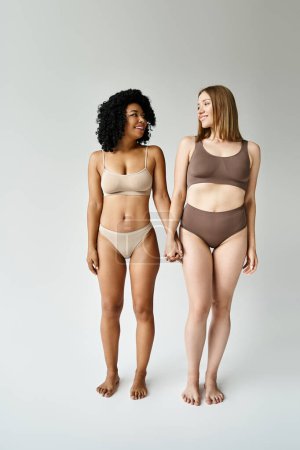 Foto de Dos mujeres diversas en bikinis pastel acogedores de pie juntos. - Imagen libre de derechos