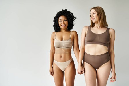 Téléchargez les photos : Two beautiful diverse women in cozy pastel bikinis standing together. - en image libre de droit