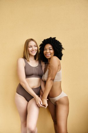 Two beautiful diverse women standing next to each other in cozy pastel underwear.