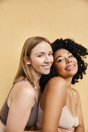 Foto de Dos hermosas mujeres diversas en acogedora ropa interior pastel posan elegantemente juntas. - Imagen libre de derechos
