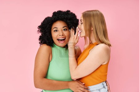 Two diverse women in casual attire pose gracefully against a soft pink backdrop.