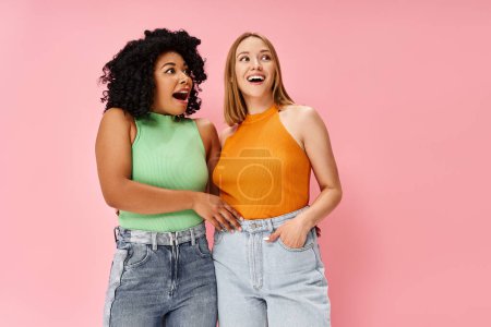 Photo for Two beautiful, diverse women in cozy casual attire stand side by side in front of a pink background. - Royalty Free Image