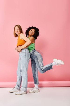 Photo for Two young women in casual attire hug in front of a pink wall. - Royalty Free Image