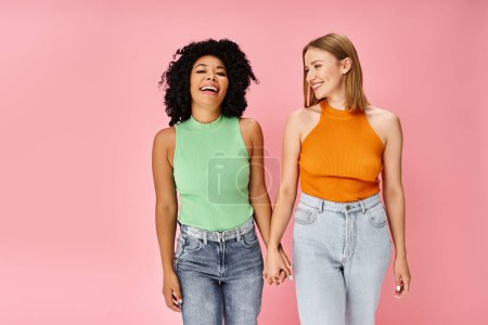 Two diverse women in stylish casual attire stand in front of a pink backdrop.