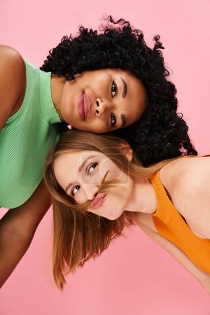 Two stylish women striking a pose in front of a pink background.