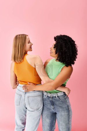 Foto de Dos mujeres diversas en traje casual acogedor de pie uno al lado del otro frente a un fondo rosa. - Imagen libre de derechos