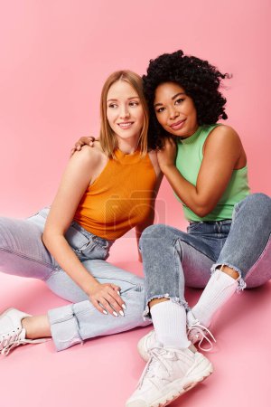 Two diverse women in casual attire sitting on the ground, striking a pose for a picture.