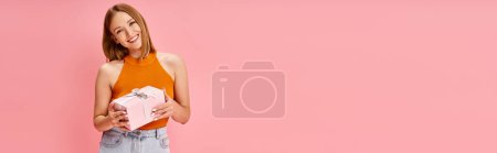 Photo for A woman in an orange top happily holding a wrapped present. - Royalty Free Image