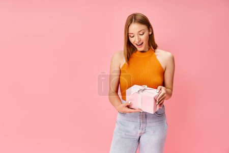 Photo for A woman in cozy casual attire holds a pink gift box in her hands. - Royalty Free Image