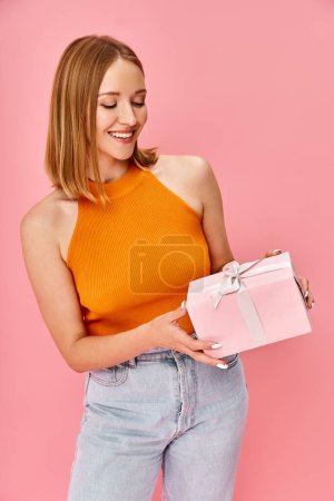 A woman in an orange top holds a white gift box.