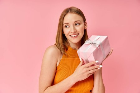 Photo for A woman in an orange top holding a pink present box. - Royalty Free Image