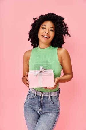 A woman in a green shirt holds a pink gift box.