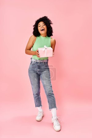 Téléchargez les photos : Une jeune femme en tenue décontractée tient joyeusement une boîte cadeau rose. - en image libre de droit