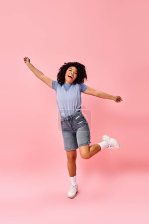 Foto de Mujer afroamericana en traje acogedor salta en el aire con los brazos extendidos. - Imagen libre de derechos
