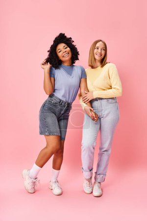 Two diverse women in casual attire stand together against a vibrant pink backdrop.