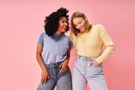 Two diverse women stand stylishly in front of a pink backdrop.