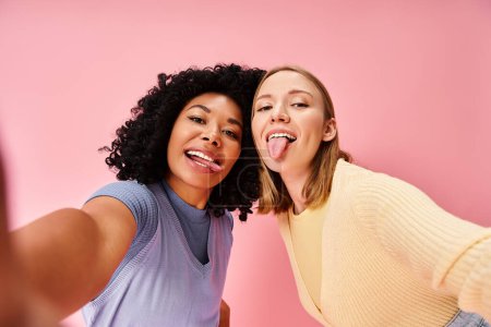 Foto de Dos mujeres en atuendo casual tomando una selfie frente a una pared rosa. - Imagen libre de derechos