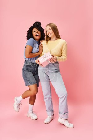 Dos mujeres diversas posan juntas en atuendo casual contra un telón de fondo rosa.