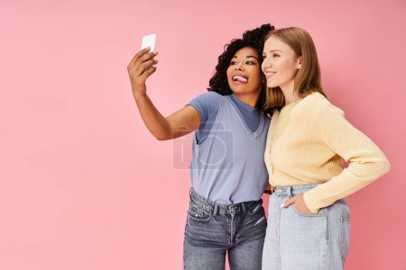 Two attractive diverse women in casual attire taking a selfie with a cell phone.