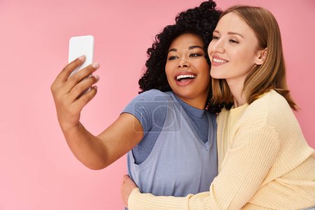 Photo for Two attractive women in casual attire taking a selfie with a cell phone. - Royalty Free Image