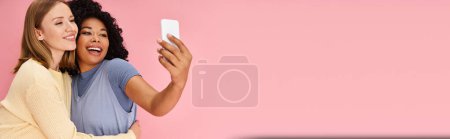 Téléchargez les photos : Deux femmes diverses en tenue décontractée prenant un selfie avec un téléphone portable. - en image libre de droit