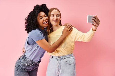 Foto de Dos atractivas y diversas mujeres en un acogedor atuendo casual tomando una selfie con un teléfono celular. - Imagen libre de derechos