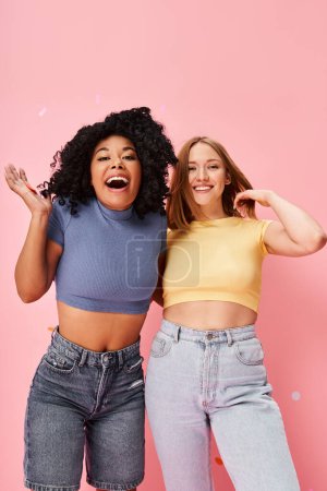 Photo for Two diverse women in casual attire standing together against a pink background. - Royalty Free Image