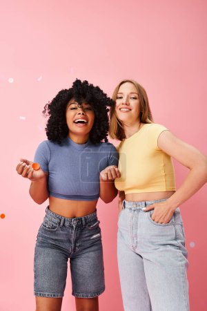 Two diverse women stand confidently in front of a vibrant pink wall.