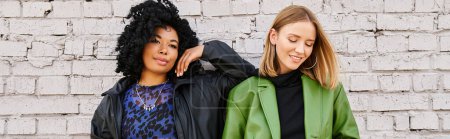 Two diverse and stylish women standing in front of a brick wall.