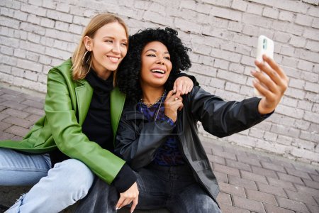 Téléchargez les photos : Deux jolies femmes en tenue décontractée prenant un selfie avec un téléphone portable. - en image libre de droit