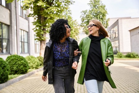 Two stylish women walking and chatting animatedly along a city sidewalk.