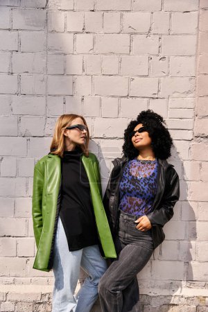 Foto de Dos mujeres diversas con atuendo casual de pie juntas frente a una pared de ladrillo. - Imagen libre de derechos