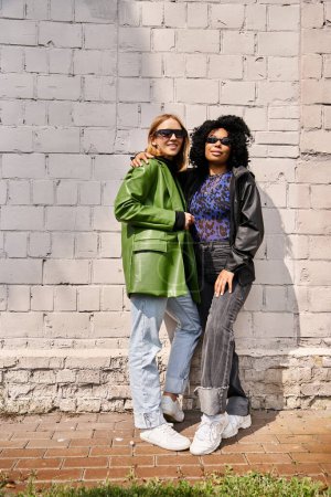 Téléchargez les photos : Deux femmes diverses en tenue décontractée confortable se tiennent côte à côte devant un mur de briques. - en image libre de droit
