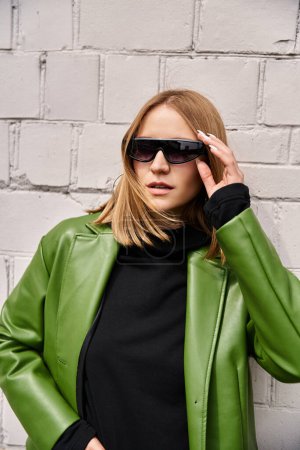 Une femme élégante respire la confiance dans une veste en cuir vert et des lunettes de soleil.