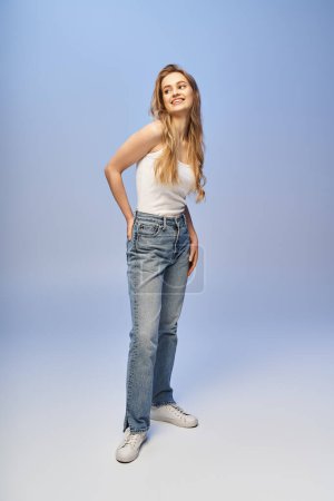 Foto de Una hermosa mujer rubia toma una pose en una camiseta sin mangas y jeans en un ambiente de estudio. - Imagen libre de derechos